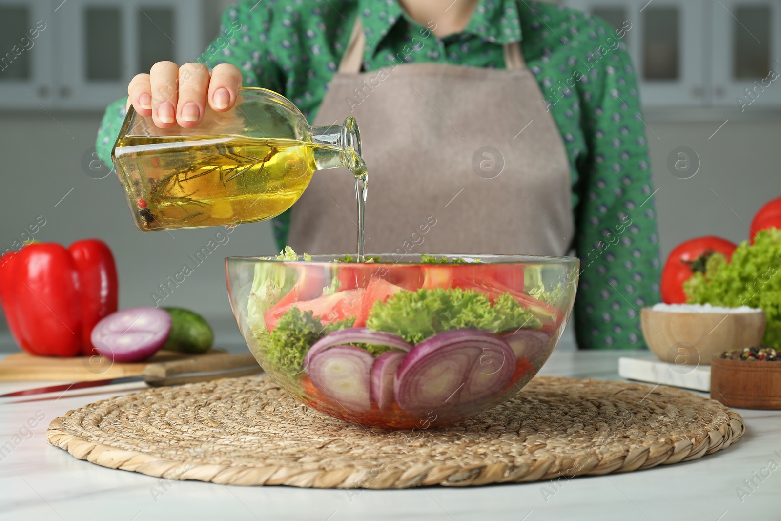 Photo of Woman pouring oil from glass bottle into bowl with salad in kitchen, closeup