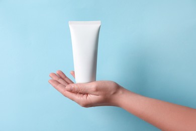 Photo of Woman with tube of hand cream on light blue background, closeup