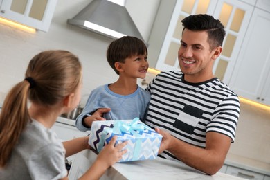 Photo of Man receiving gift for Father's Day from his children in kitchen