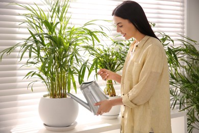 Young woman watering house plant on window sill indoors