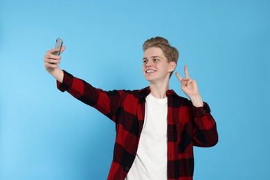 Photo of Teenage boy taking selfie on light blue background