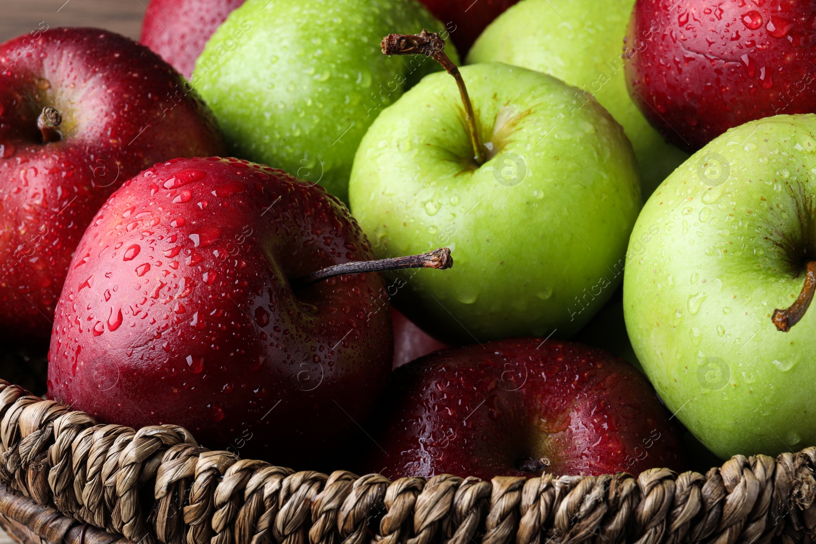 Photo of Fresh ripe green and red apples with water drops in wicker bowl, closeup