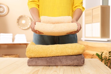 Woman stacking clean towels on wooden table in laundry room, closeup