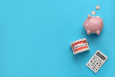 Photo of Educational dental typodont model, piggy bank and calculator on light blue background, flat lay with space for text. Expensive treatment