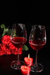 Glasses of wine, roses and heart shaped candles for romantic dinner on black table