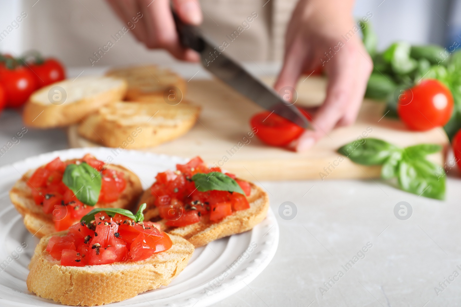 Photo of Woman cutting tomato at light grey table, focus on tasty bruschetta