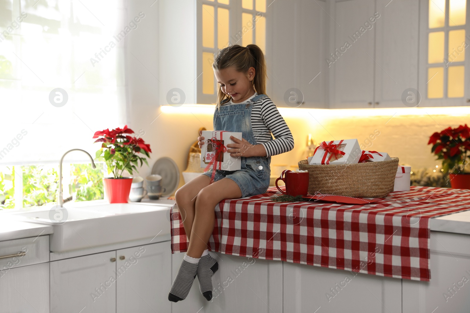 Photo of Cute little girl with gift from Christmas advent calendar on table in kitchen