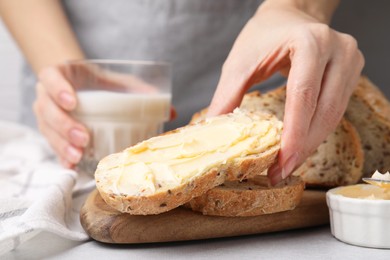 Photo of Woman taking slice of bread with tasty butter at table, closeup