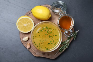 Bowl with lemon sauce and ingredients on dark table, top view. Delicious salad dressing