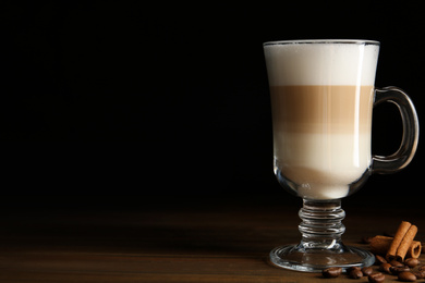 Photo of Delicious latte macchiato, cinnamon and coffee beans on wooden table against black background, space for text