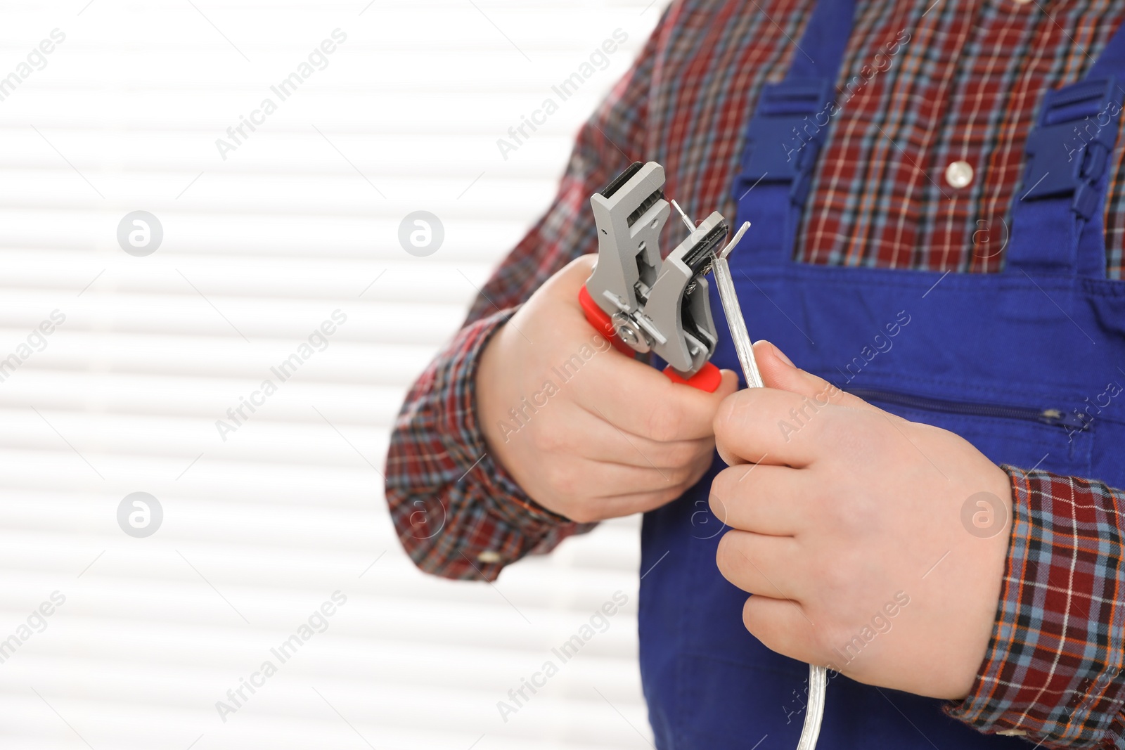 Photo of Professional electrician in uniform stripping wiring indoors, closeup