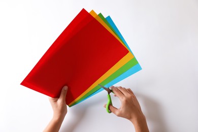 Woman cutting color sheets of paper with scissors on white background, closeup