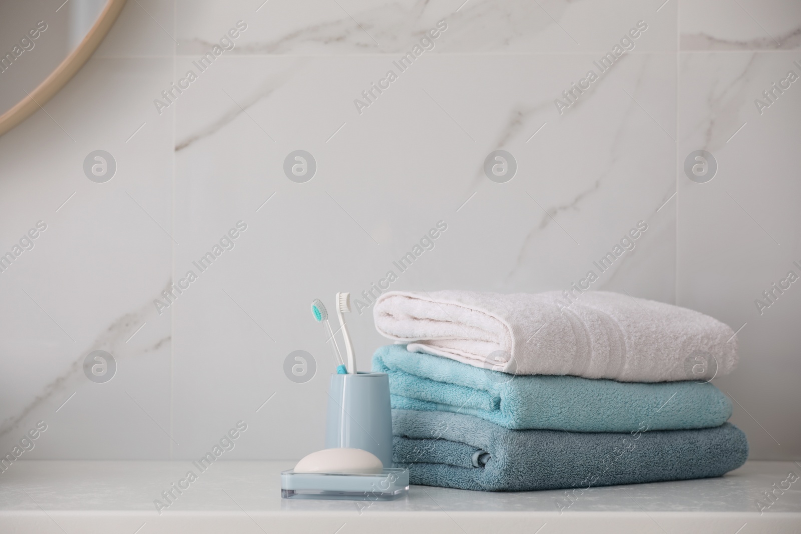 Photo of Stack of fresh towels, toothbrushes and soap bar on countertop  in bathroom. Space for text