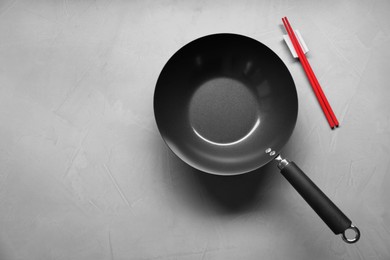 Empty wok and chopsticks on grey table, flat lay. Space for text