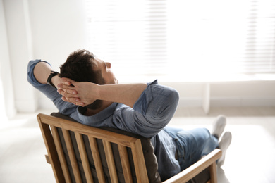 Photo of Young man relaxing in armchair near window at home