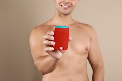 Photo of Young man holding deodorant on beige background, closeup. Mockup for design