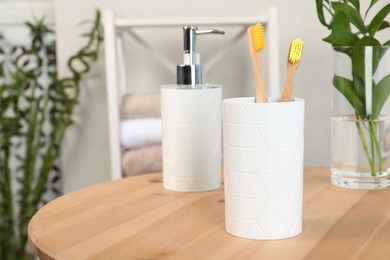 Photo of Holder with bamboo toothbrushes on table against blurred background