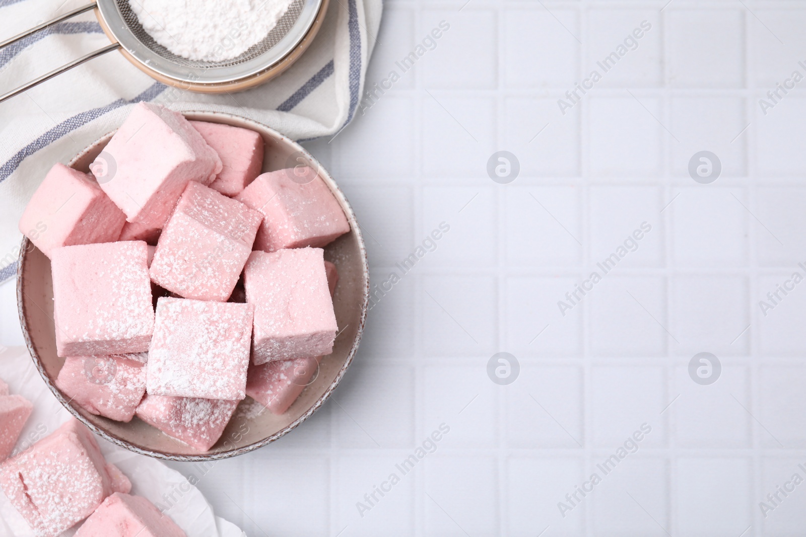 Photo of Bowl of delicious sweet marshmallows with powdered sugar on white table, flat lay. Space for text