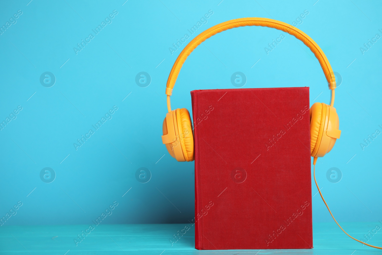 Photo of Book and modern headphones on light blue wooden table. Space for text