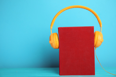 Book and modern headphones on light blue wooden table. Space for text