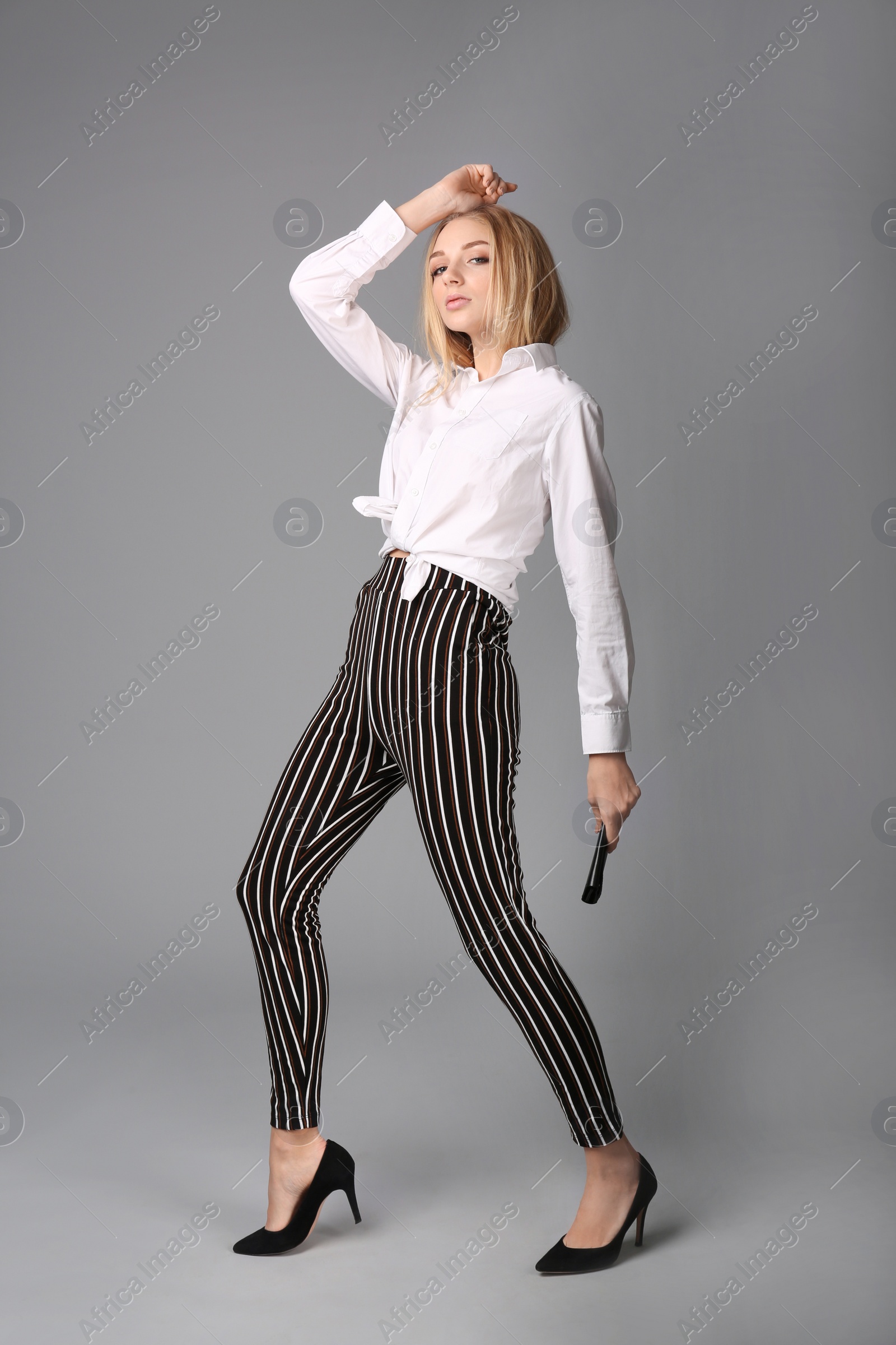 Photo of Young stylish woman in trendy shoes with bag on grey background