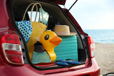 Photo of Red car with luggage on beach, closeup. Summer vacation trip