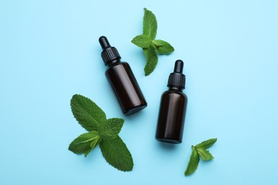 Bottles of essential oil and mint on light blue background, flat lay