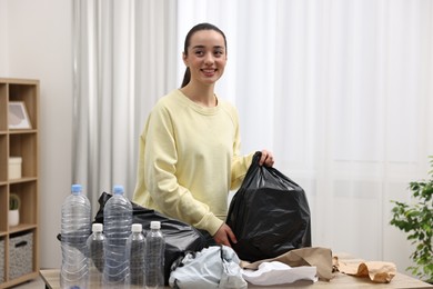 Photo of Smiling woman with plastic bag separating garbage in room