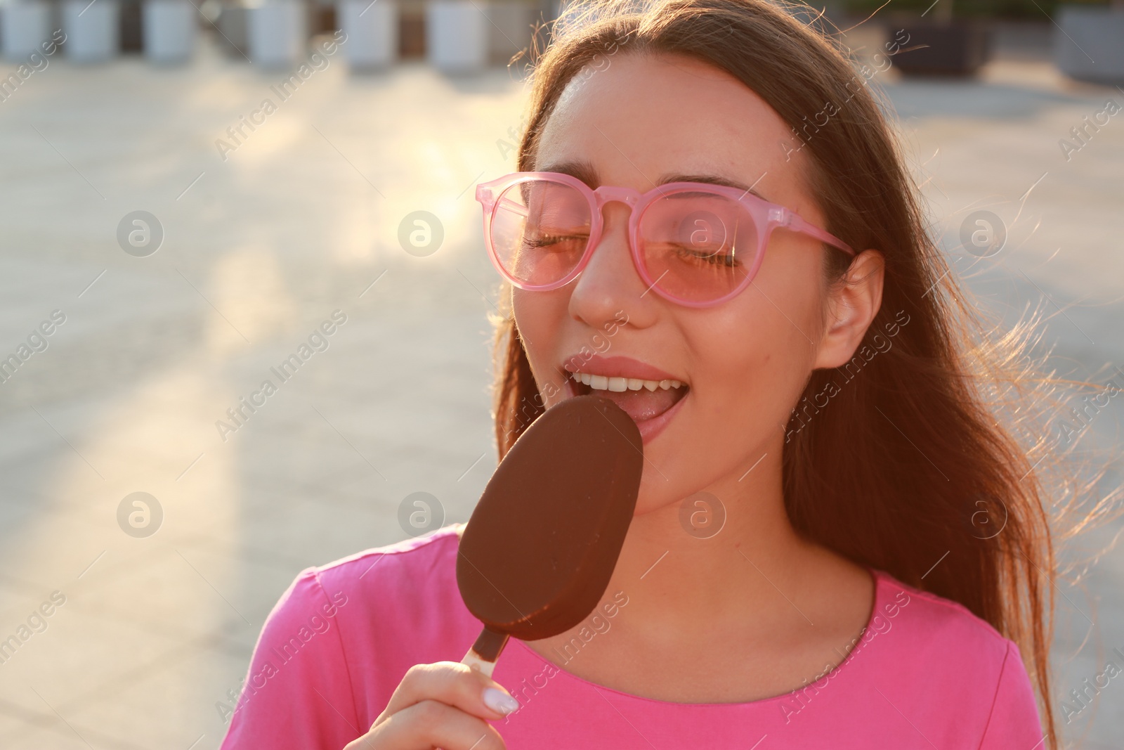 Photo of Beautiful young woman eating ice cream glazed in chocolate on city street