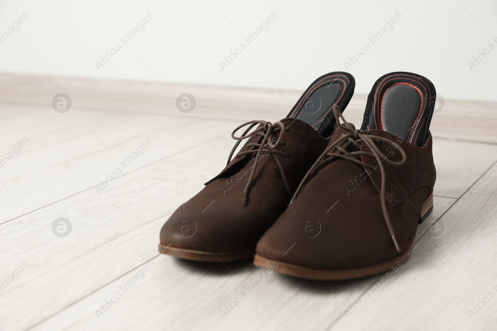 Photo of Orthopedic insoles in shoes on floor, closeup. Space for text