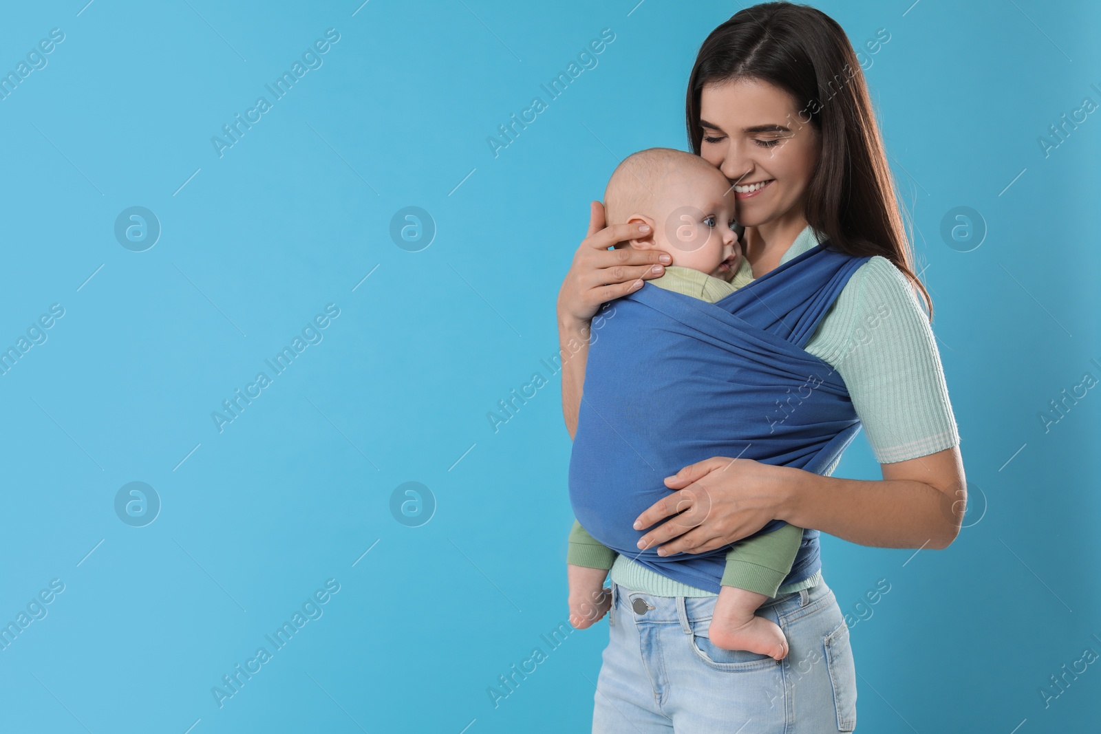 Photo of Mother holding her child in sling (baby carrier) on light blue background. Space for text