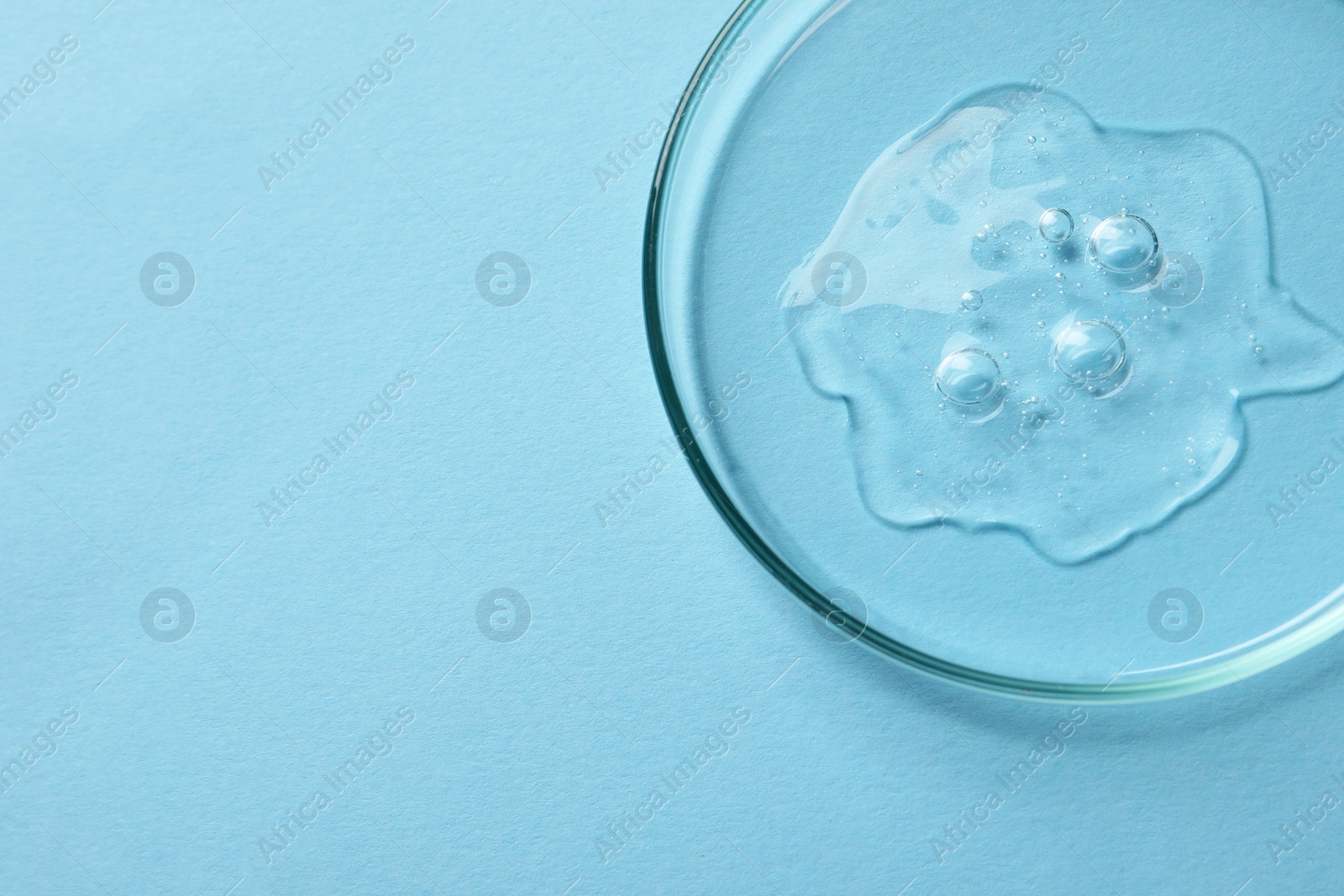 Photo of Petri dish with sample of cosmetic oil on light blue background, above view. Space for text