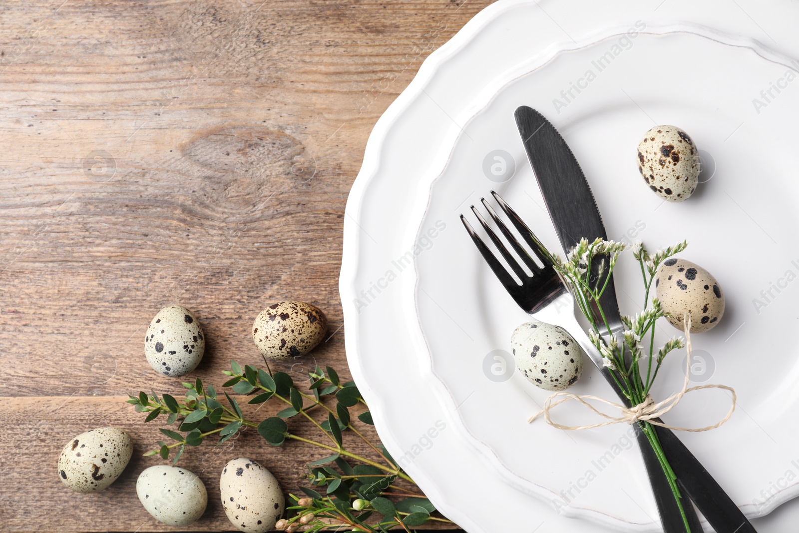 Photo of Festive Easter table setting with quail eggs and floral decor on wooden background, top view