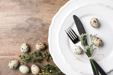 Festive Easter table setting with quail eggs and floral decor on wooden background, top view