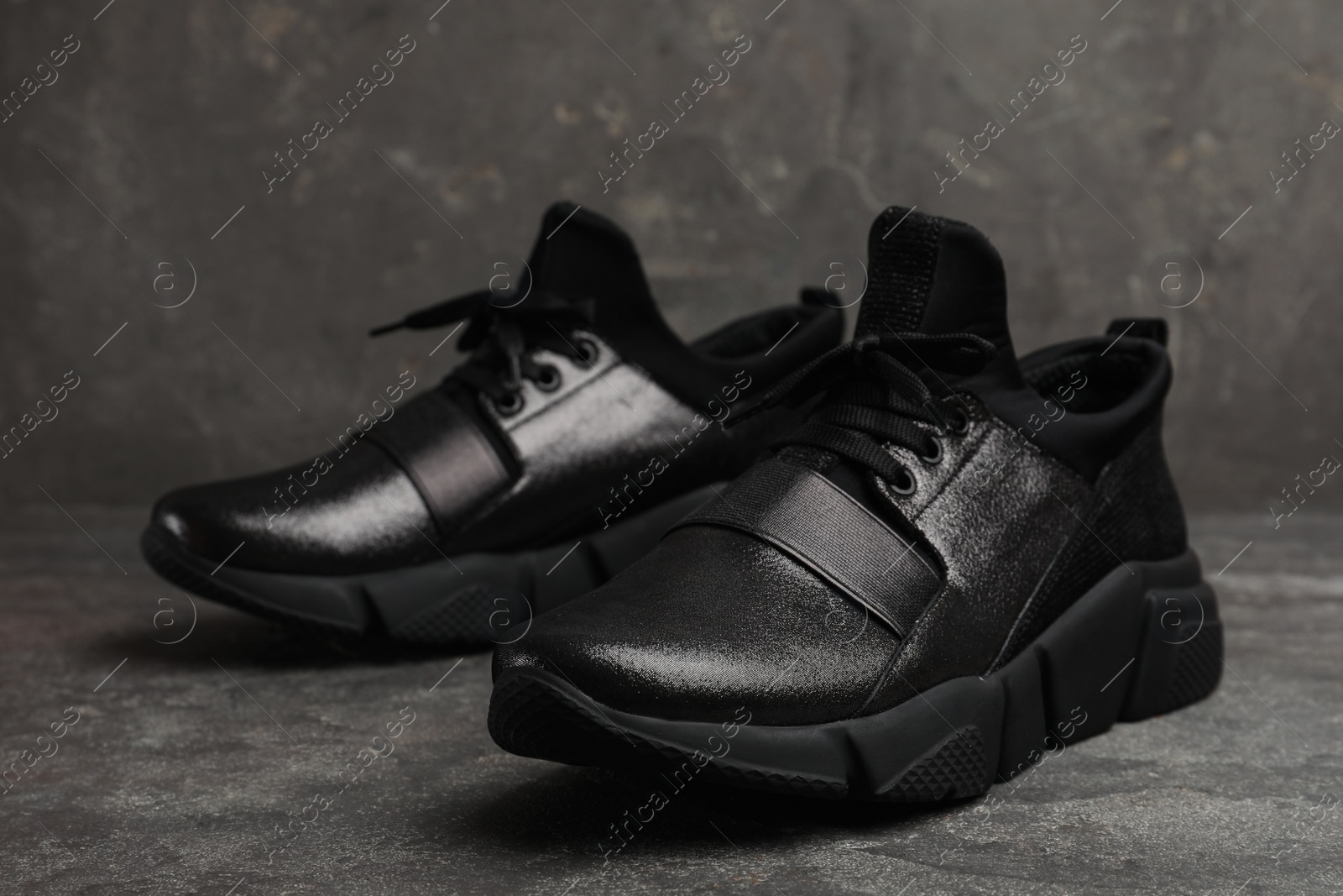 Photo of Stylish black sneakers on grey stone table, closeup