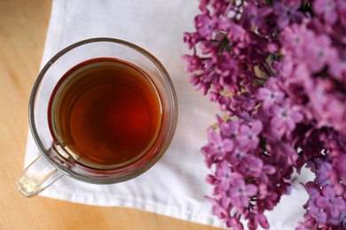 Photo of Beautiful lilac flowers and glass cup of tea on wooden table, top view