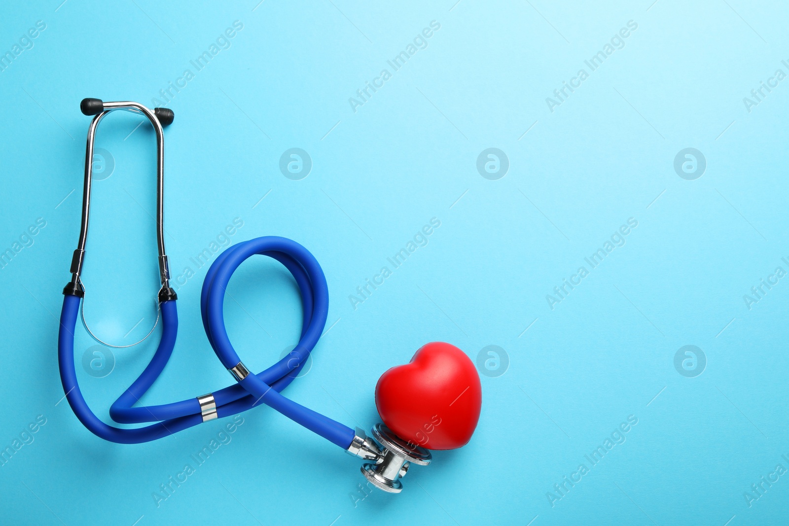 Photo of Stethoscope and red heart on light blue background, top view. Space for text