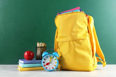 Backpack with school stationery on table against blackboard