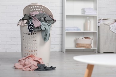 Plastic laundry basket overfilled with clothes indoors. Space for text