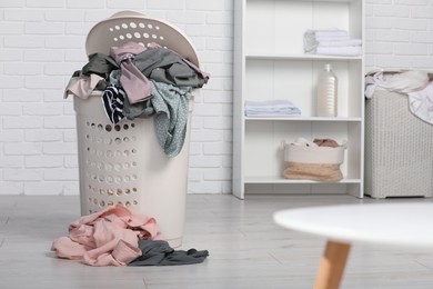 Photo of Plastic laundry basket overfilled with clothes indoors. Space for text