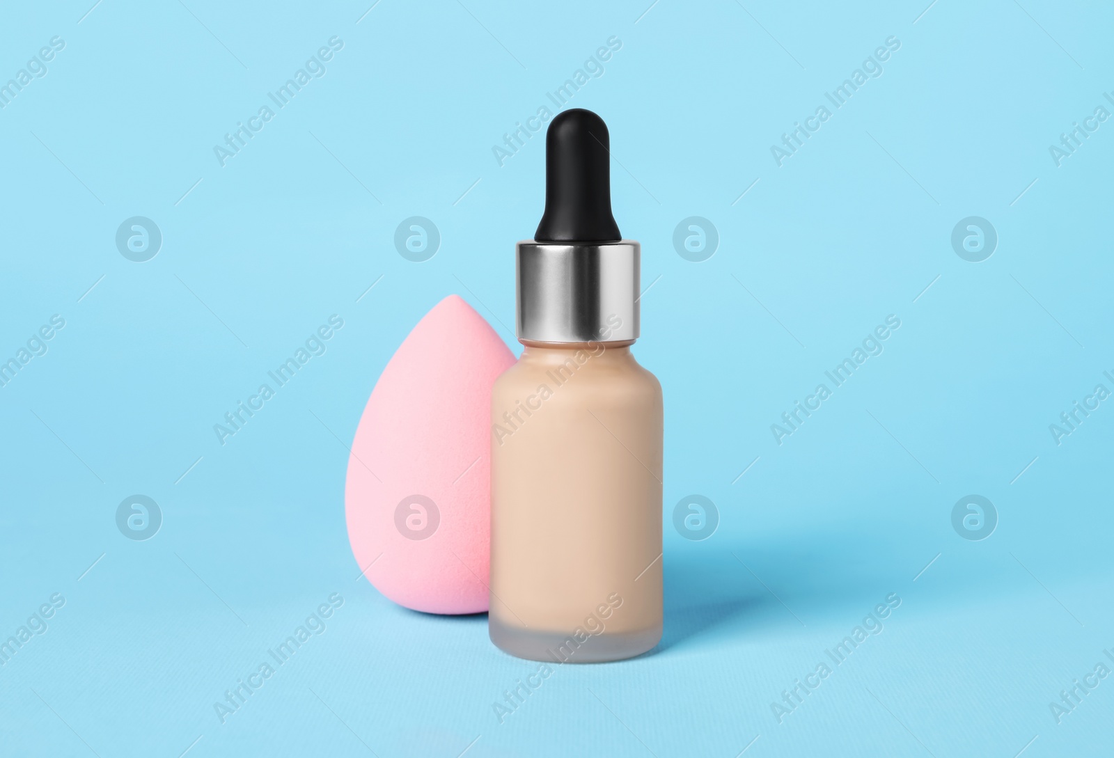 Photo of Bottle of skin foundation and sponge on light blue background. Makeup product