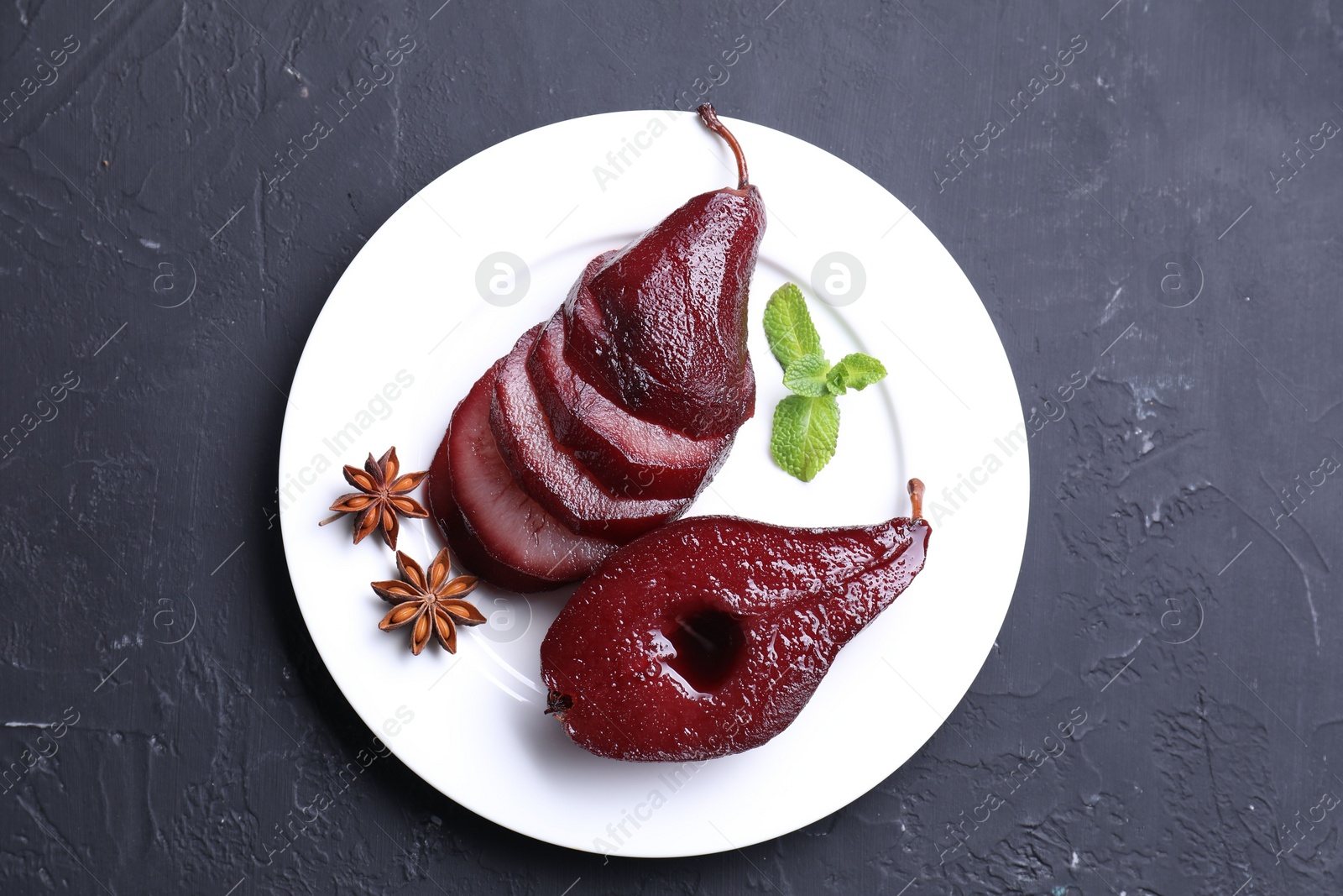 Photo of Tasty red wine poached pears, mint and anise on black table, top view