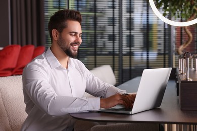 Happy young man working on laptop at table in office