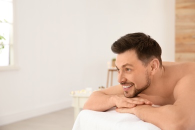 Handsome man relaxing on massage table in spa salon, space for text