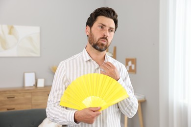 Bearded man with hand fan suffering from heat at home