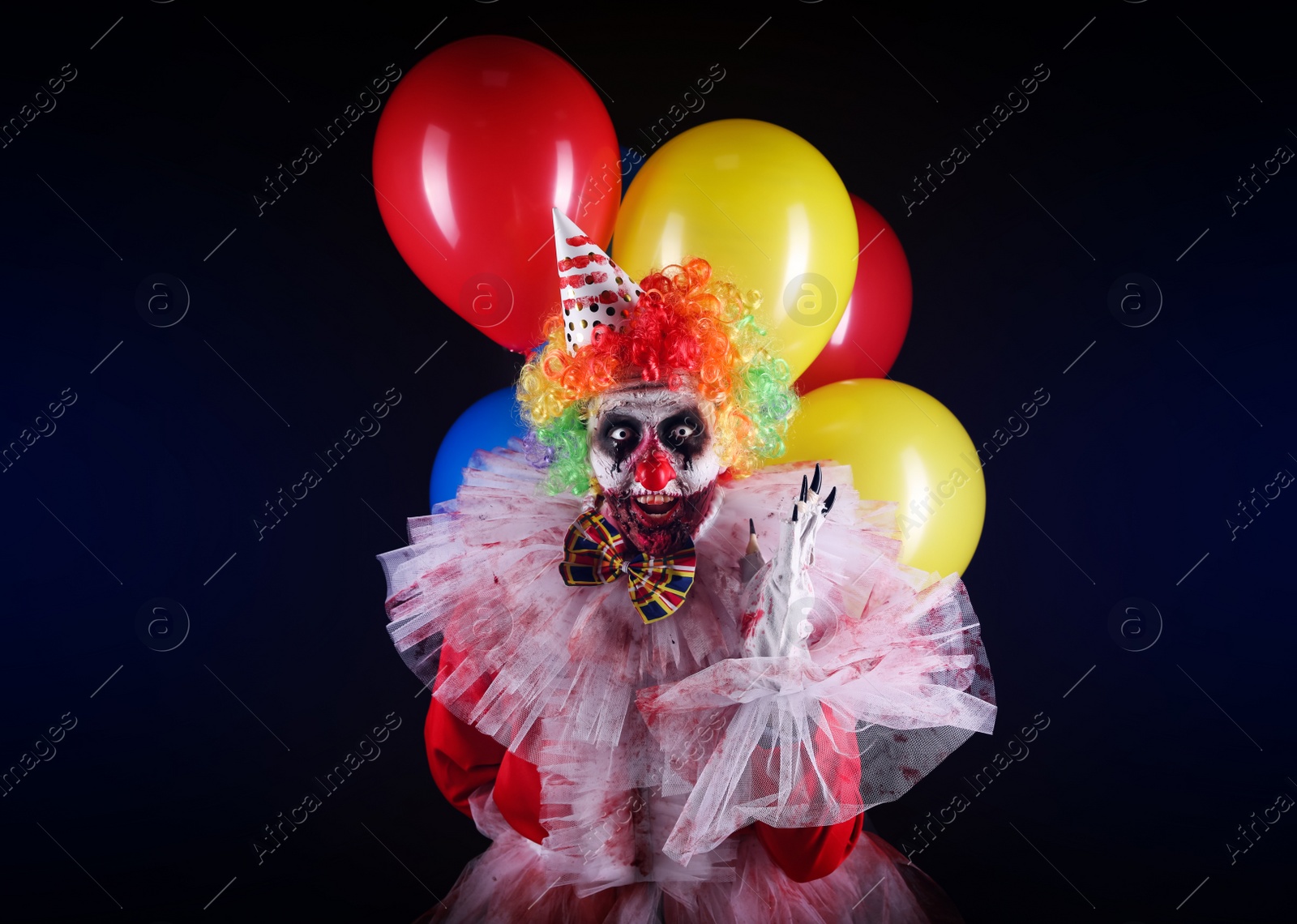 Photo of Terrifying clown with air balloons on dark background. Halloween party costume