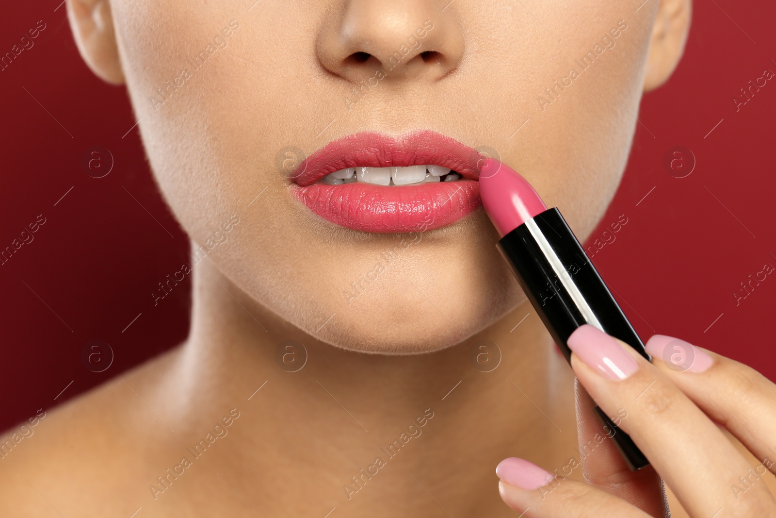 Photo of Young woman applying lipstick on color background, closeup