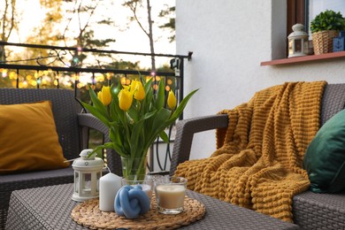 Photo of Soft pillows, blanket, candles and yellow tulips on rattan garden furniture outdoors