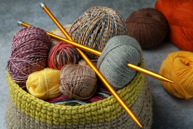Soft woolen yarns and knitting needles on grey table, closeup