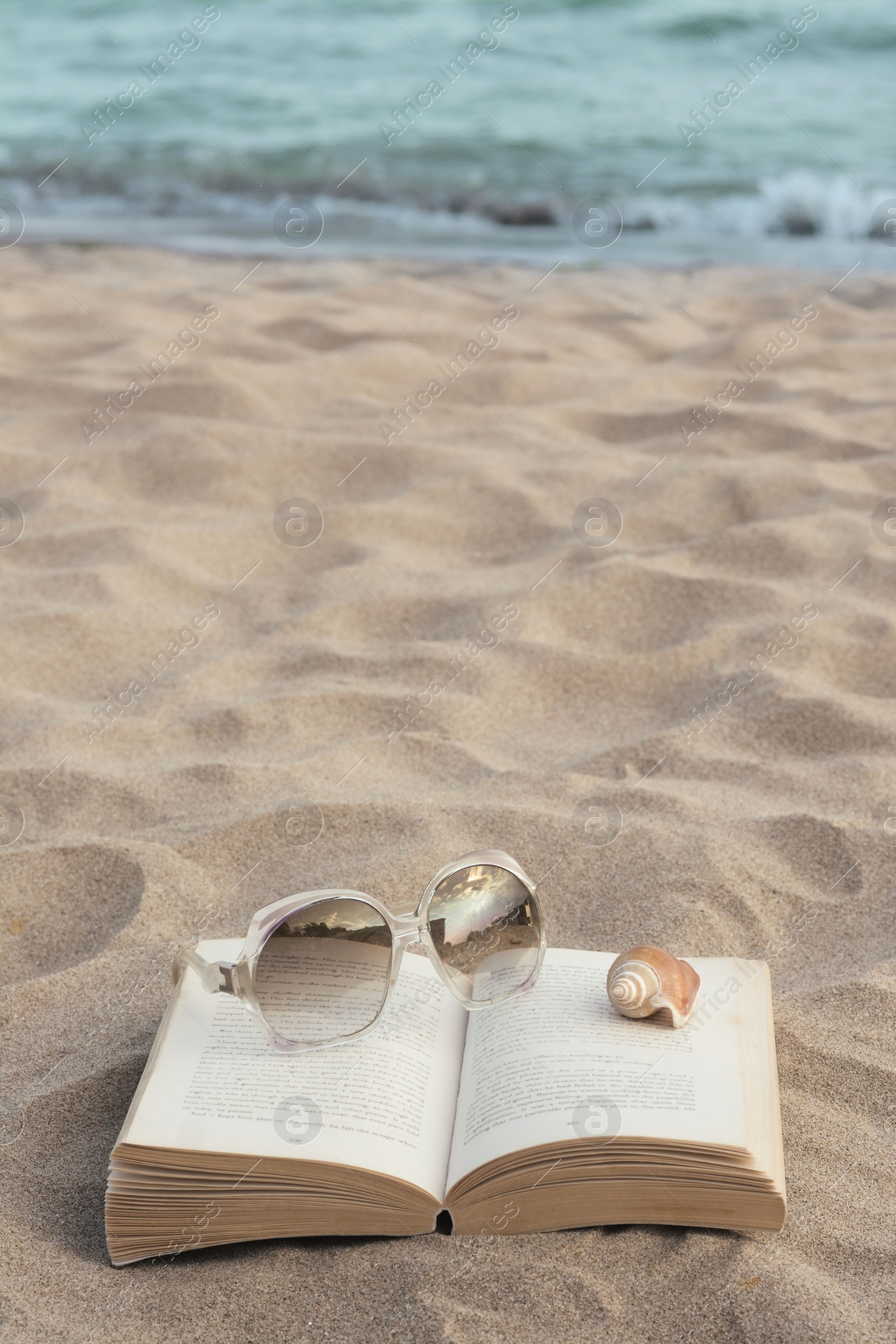 Photo of Beautiful sunglasses, book and shell on sand near sea, space for text